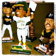 Oakland A's stadium giveaway bobbleheads on a shelf, with Rickey Henderson in front and Jason Giambi beside him